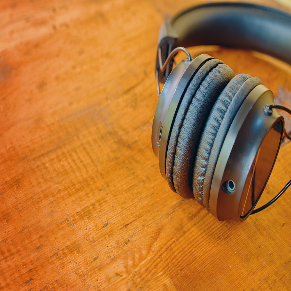 Wireless headphones close-up. Black earphones on wooden table. Copy space for text. Modern gadgets. Concept of music and podcasting.